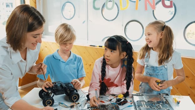 Young smart caucasian teacher teaching diverse students about electronic board. Multicultural children learn about digital electrical tool and fixing motherboard by using chips and wires. Erudition.