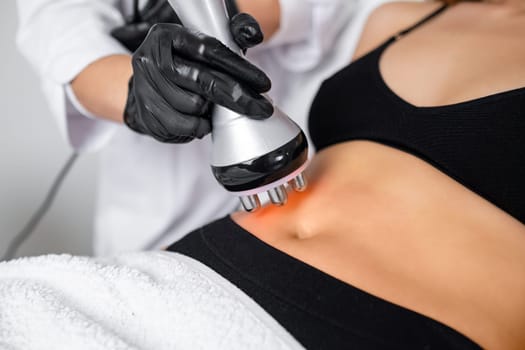 A young woman receives RF body cavitation lifting treatment at a beauty salon to target belly fat reduction.