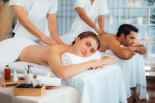 Caucasian couple customer enjoying relaxing anti-stress spa massage and pampering with beauty skin recreation leisure in day light ambient salon spa at luxury resort or hotel. Quiescent