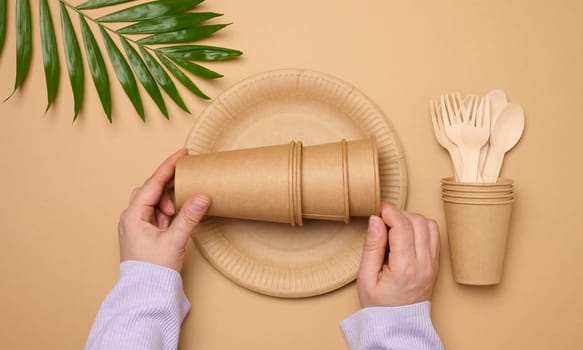 Paper plates and cups, wooden spoons and forks on a beige background, top view