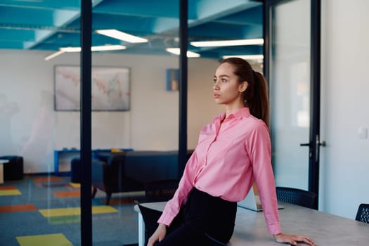 Portrait of young smiling business woman in creative open space coworking startup office. Successful businesswoman standing in office with copyspace. Coworkers working in background.