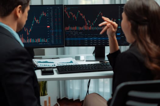 Two business traders discussing on dynamic stock market in currency rate investment trading on two pc screens with compare real time graph on risk or profit point of data at modern office. Postulate.