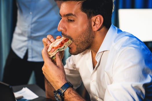 Coworker partners with happy face eating sandwich and drinking coffee while working job project at night time. Creative freelancers getting e-mail bidding winner online network application. Sellable.