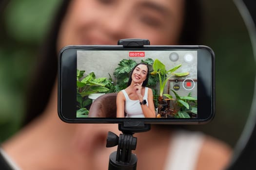 Rear view woman make natural beauty and cosmetic tutorial on green plant garden video content display on phone screen. Beauty blogger showing how to beauty care to social medial audience. Blithe