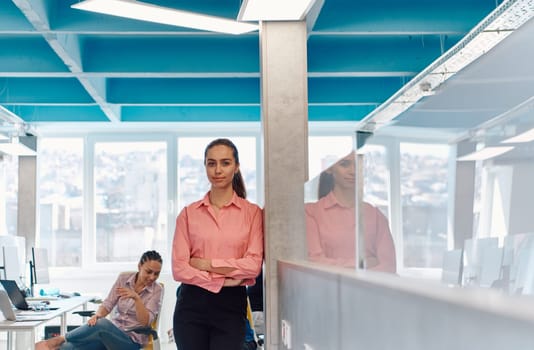 Portrait of young smiling business woman in creative open space coworking startup office. Successful businesswoman standing in office with copyspace. Coworkers working in background.