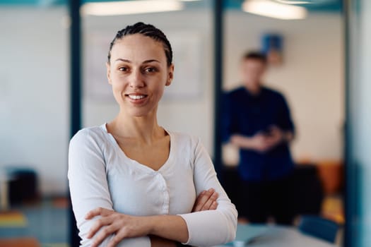 Portrait of a business woman in a creative open space coworking startup office with crossed arms. Successful businesswoman standing in office with copyspace. Associates work in the background.