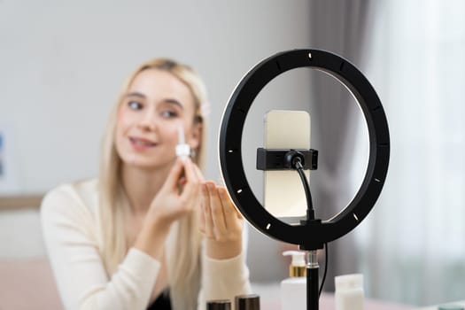 Young woman making beauty and cosmetic tutorial video content for social media. Beauty blogger smiles to camera while showing how to apply beauty skincare to audience or followers. Blithe