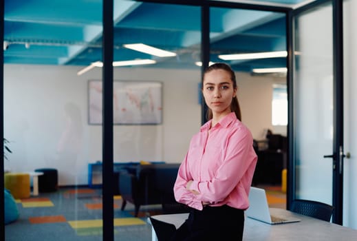 Portrait of a business woman in a creative open space coworking startup office with crossed arms. Successful businesswoman standing in office with copyspace. Associates work in the background.