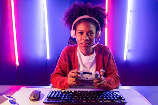 Host channel of gaming streamer, African girl playing online game with joystick, talking with viewers media online on microphone. Esport skilled team players in neon color lighting room. Tastemaker.