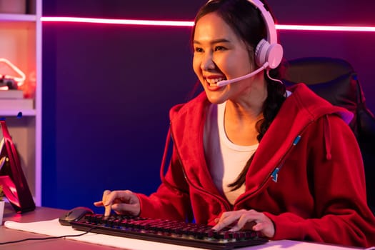 Host channel of smiling beautiful Asian girl streamer playing online game wearing headphone talking with viewers media online recording phone. Esport skilled team players in neon blue room. Stratagem.