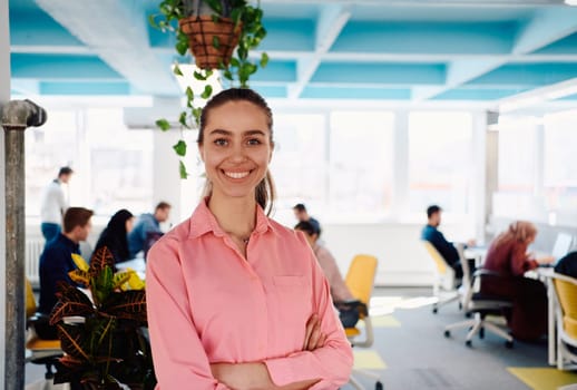 Portrait of young smiling business woman in creative open space coworking startup office. Successful businesswoman standing in office with copyspace. Coworkers working in background.