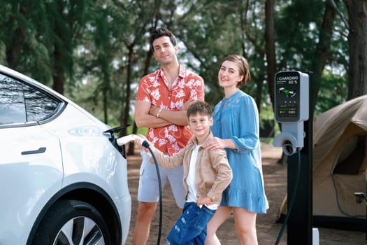 Outdoor adventure and family vacation camping in nature travel by eco friendly car for sustainable future. Lovely family recharge EV car with EV charging station in campsite. Perpetual