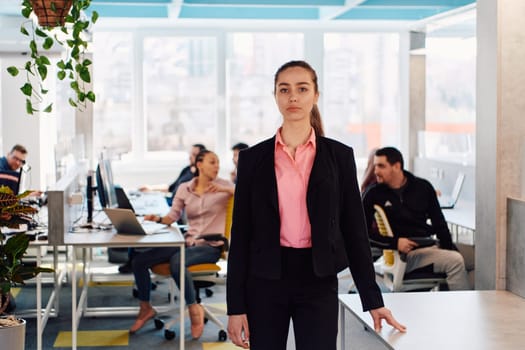 Portrait of young smiling business woman in creative open space coworking startup office. Successful businesswoman standing in office with copyspace. Coworkers working in background.