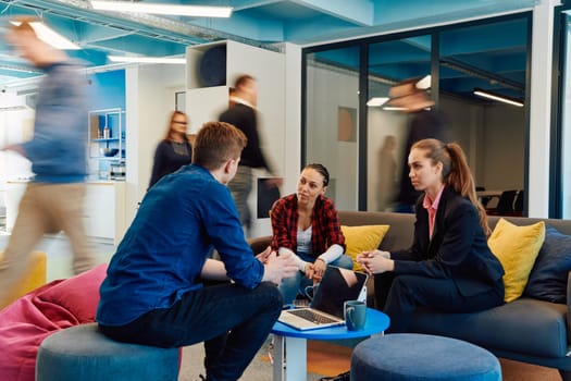 Multiethnic startup business team on meeting in a modern bright open space coworking office. Brainstorming, working on laptop. Group of coworkers walking around in motion blur.