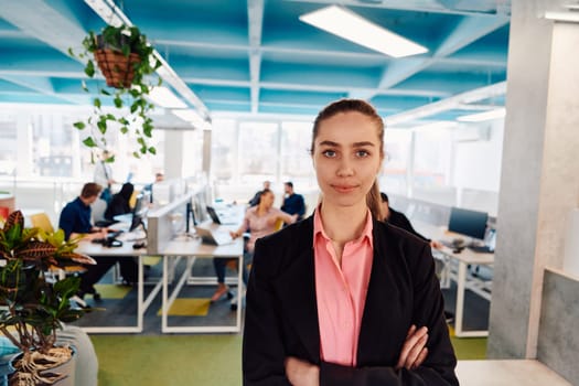 Portrait of young smiling business woman in creative open space coworking startup office. Successful businesswoman standing in office with copyspace. Coworkers working in background.