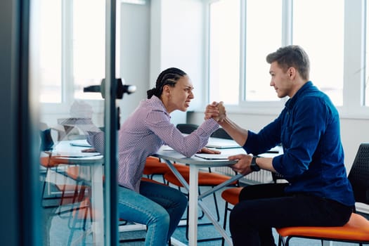 In a modern startup office, a businessman and a businesswoman business colleagues engage in a symbolic arm-wrestling match, reflecting teamwork, competition, and innovation in their dynamic workplace