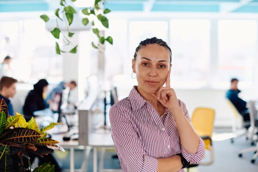 Portrait of young smiling business woman in creative open space coworking startup office. Successful businesswoman standing in office with copyspace. Coworkers working in background.