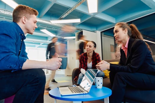 Multiethnic startup business team on meeting in a modern bright open space coworking office. Brainstorming, working on laptop. Group of coworkers walking around in motion blur.