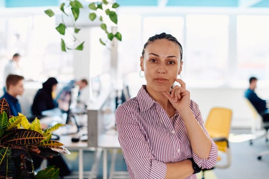 Portrait of young smiling business woman in creative open space coworking startup office. Successful businesswoman standing in office with copyspace. Coworkers working in background.