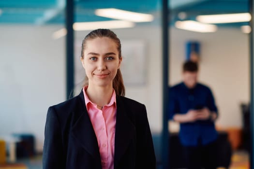 Portrait of young smiling business woman in creative open space coworking startup office. Successful businesswoman standing in office with copyspace. Coworkers working in background.