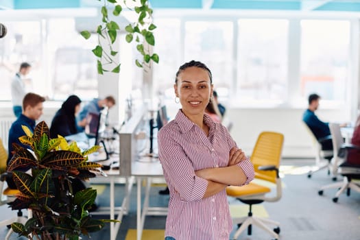 Portrait of young smiling business woman in creative open space coworking startup office. Successful businesswoman standing in office with copyspace. Coworkers working in background.