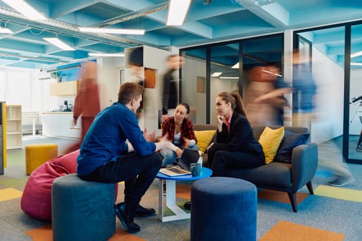 Multiethnic startup business team on meeting in a modern bright open space coworking office. Brainstorming, working on laptop. Group of coworkers walking around in motion blur.