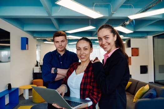 A young team of business professionals poses for a startup office portrait, exuding confidence and ambition, with one woman holding a laptop, symbolizing innovation and collaboration in entrepreneurship.