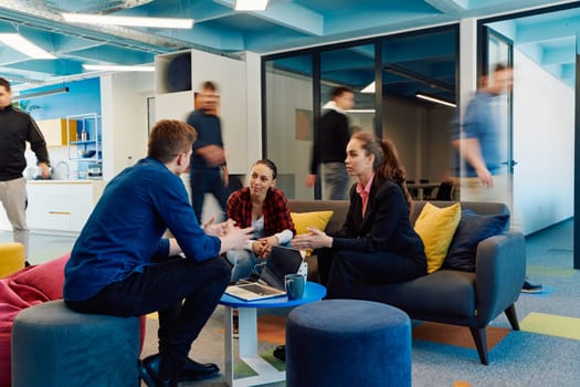 Multiethnic startup business team on meeting in a modern bright open space coworking office. Brainstorming, working on laptop. Group of coworkers walking around in motion blur.