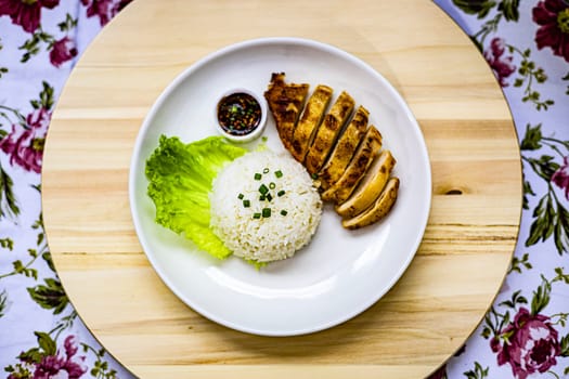 Top view of roasted chicken breast fillet steak with rice, vegetables salad and spicy sauce in white plate on wooden table. 