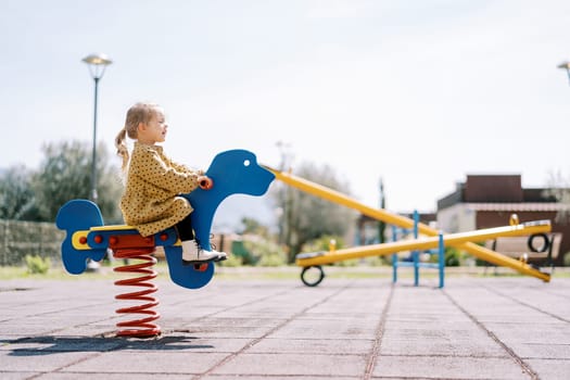 Little girl swings on a spring swing on the playground. Side view. High quality photo