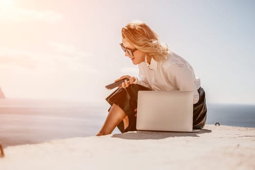 Digital nomad, Business woman working on laptop by the sea. Pretty lady typing on computer by the sea at sunset, makes a business transaction online from a distance. Freelance remote work on vacation