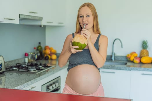 Quenching her pregnancy thirst with a refreshing choice, a pregnant woman joyfully drinks coconut water from a coconut in the kitchen, embracing natural hydration during this special journey.