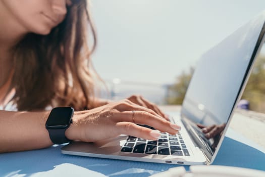 Digital nomad, Business woman working on laptop by the sea. Pretty lady typing on computer by the sea at sunset, makes a business transaction online from a distance. Freelance, remote work on vacation