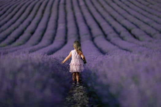 Lavender field girl. Back view happy girl in pink dress with flowing hair runs through a lilac field of lavender. Aromatherapy travel.