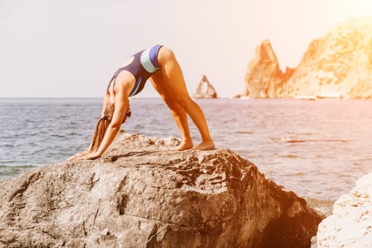 Yoga on the beach. A happy woman meditating in a yoga pose on the beach, surrounded by the ocean and rock mountains, promoting a healthy lifestyle outdoors in nature, and inspiring fitness concept