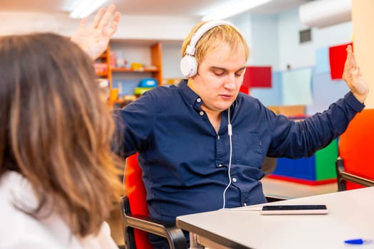 Man with mental disability listening to music using headphones next to a friend in a day center