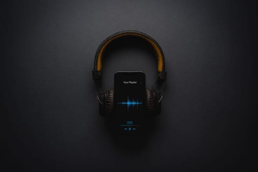 Smartphone with music player app and on-ear headphones on dark gray background