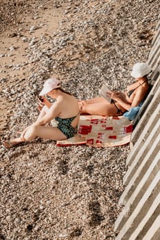 Beautiful Young Woman reading book and Sitting on the Beach Chair Under Beach Umbrella on Vacation. Summer Holidays Travel Concept.