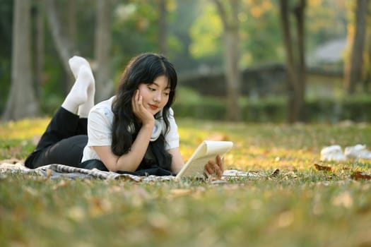 Peaceful young woman relaxing on green grass and reading book.