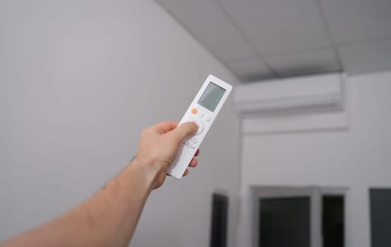 Hand with the remote control is directed to air conditioner. Climate control in office or at home concept