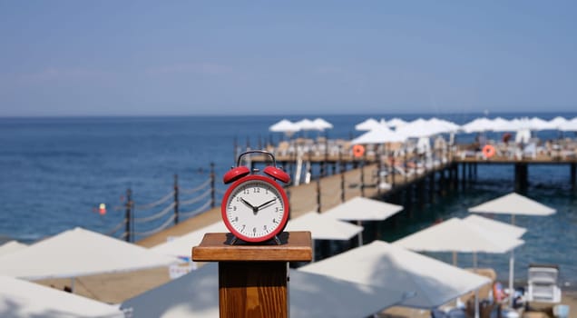 Alarm clock for ten o'clock on beach with jetty and umbrellas. Summer vacation time tourism and travel to sea