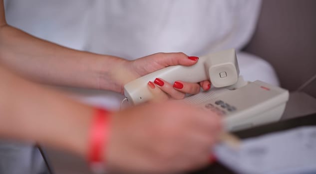 Woman dials phone number in the hotel rooms to communicate with reception. Contact us concept