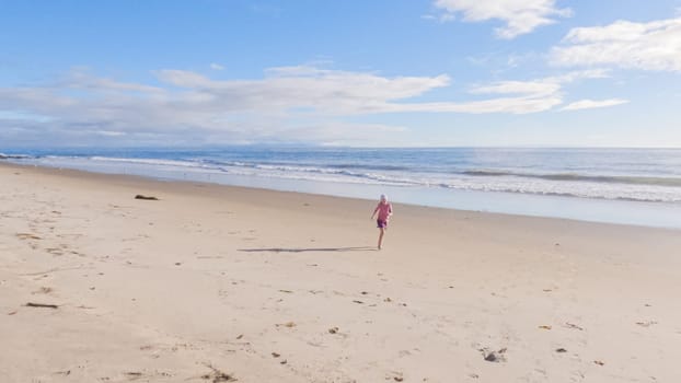 A little girl joyfully plays on the vast, empty sands of El Capitan State Beach in California during winter.