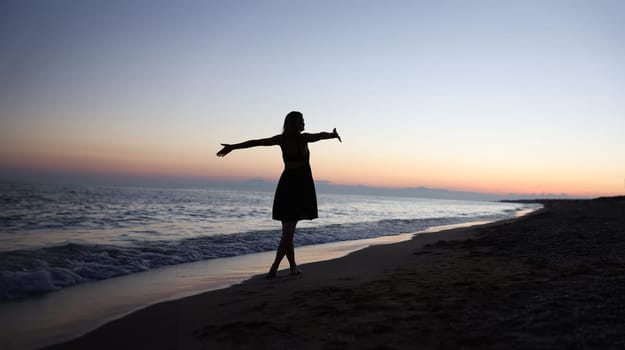 Woman standing with open arms on seashore at sunset. Beautiful life concept
