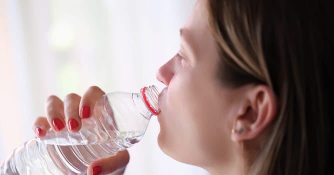 Young woman drinks water from bottle. Water benefits for skin and health concept