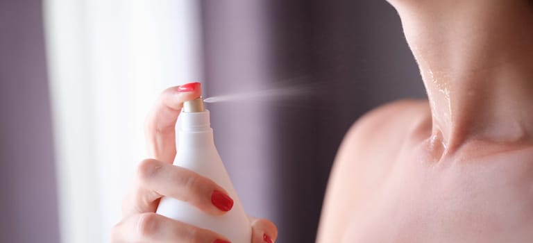 Woman spraying perfume or moisturizing skin lotion on neck closeup. Neck care concept