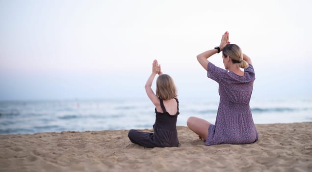 Happy family mother and daughter do yoga, meditate in lotus position on beach. Relaxation, relaxation and harmony with nature