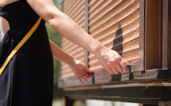 Female hands hold wooden latch handles open wooden blinds outdoors closeup. Roller blind opening concept