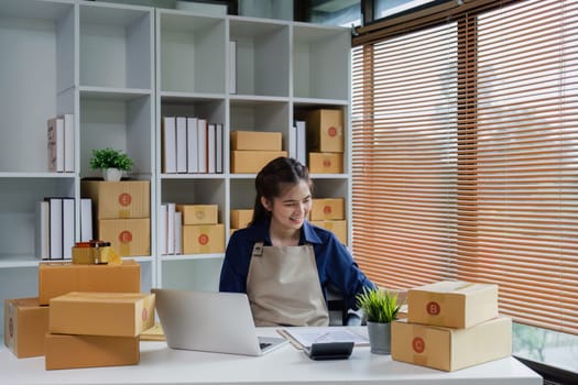 Startup small business entrepreneur woman using a laptop for prepare package with box to client.