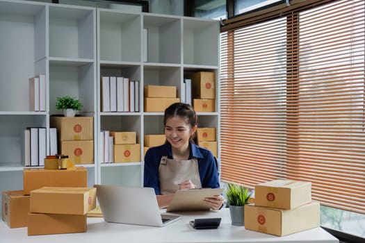 Startup small business entrepreneur woman using a laptop for prepare package with box to client.